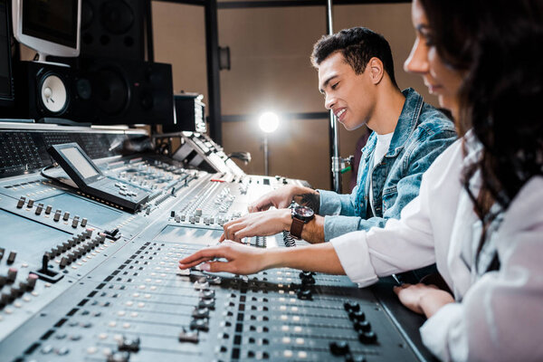 two young multicultural sound producers working at mixing console i recording studio