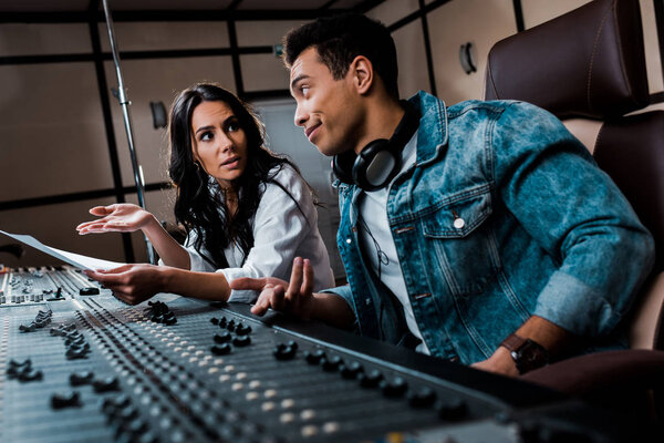 two quarrelling multicultural sound producers working at mixing console in recording studio