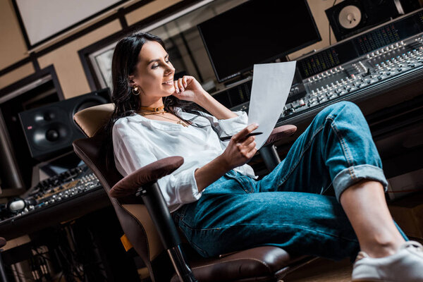 beautiful smiling sound producer sitting in office chair near mixing console in recording studio