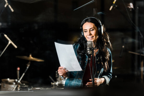 beautiful woman in headphones singing in recording studio near microphone
