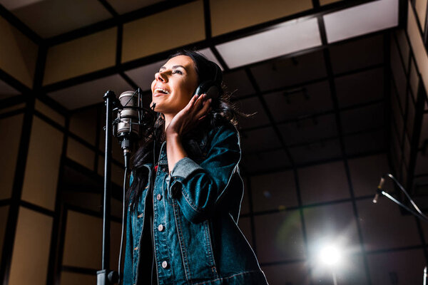 beautiful inspired woman singing near microphone in dark recording studio