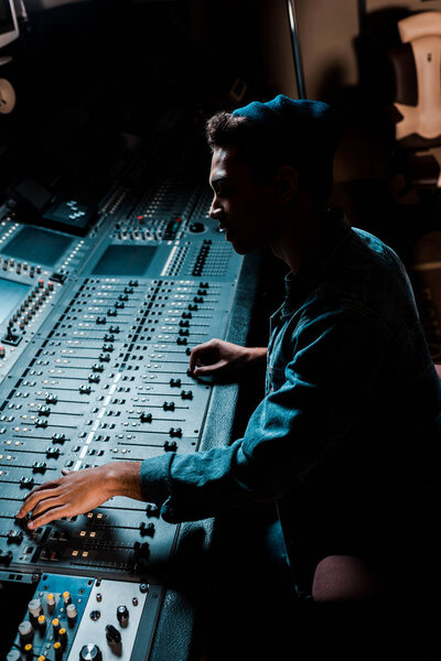 sound producer working at mixing console in dark recording studio