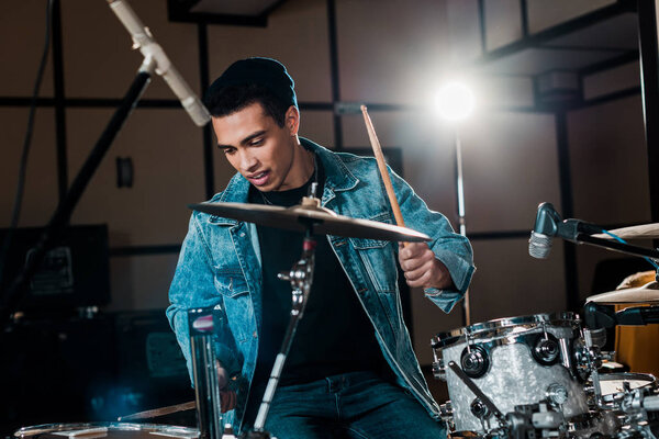 красивый, вдохновленный музыкант смешанной расы, играющий на барабанах в студии звукозаписи
