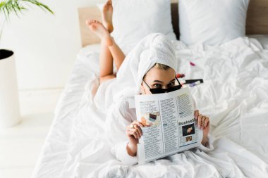 gömlek şık yalınayak kadın, güneş gözlüğü, takı ve yatakta baş okuma iş gazetesi havlu ile