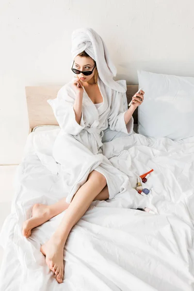 バスローブとサングラス タオル ジュエリーをベッドに寝かせ スマートフォンを使用してスタイリッシュな女性 — ストック写真