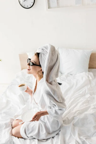 快乐时尚的女人在浴袍和太阳镜 毛巾和珠宝在床上喝咖啡 — 图库照片