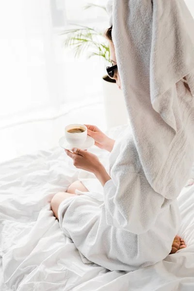 穿着浴袍和太阳镜 毛巾和珠宝的时尚女士在床上拿着咖啡杯 — 图库照片