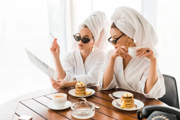 穿着浴袍 太阳镜和珠宝的时尚女性 头上有毛巾 一边抽烟一边看报纸 一边吃早餐 — 图库照片