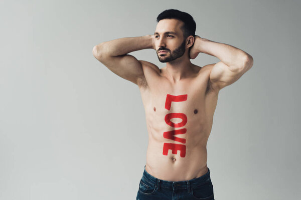 Shirtless dreamy man with inscription on body posing with hands up isolated on grey