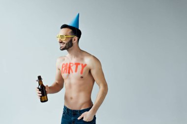 Parti şapkasındaki adam bira tutuyor ve griye bakıyor.