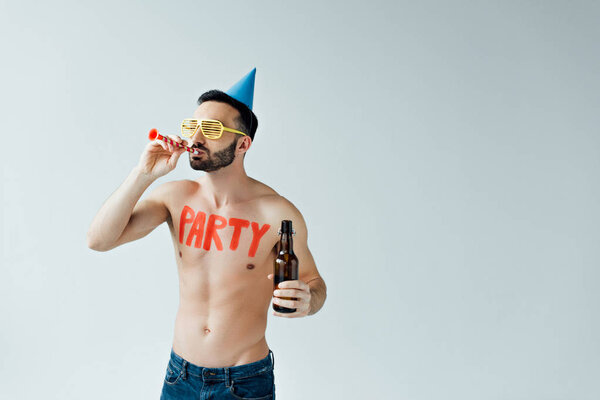 Shirtless man with party blower holding bottle of beer isolated on grey
