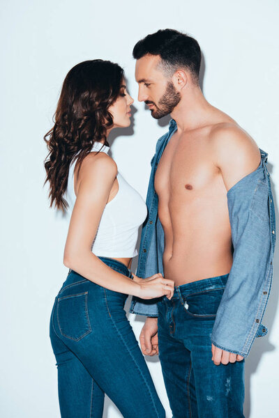sensual young woman unzipping jeans on boyfriend on grey