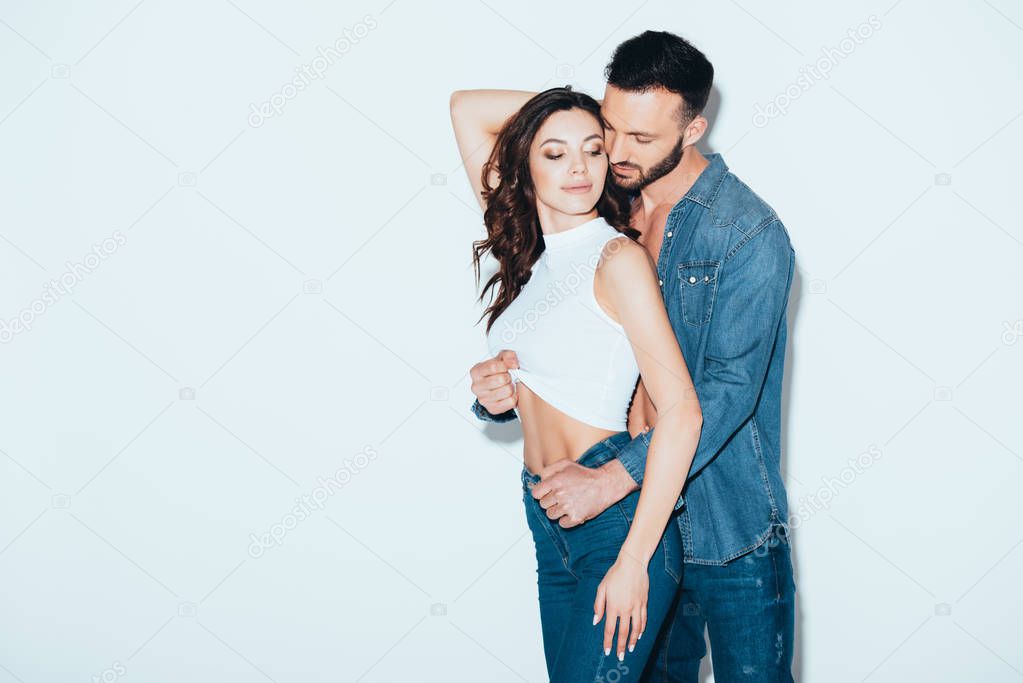 bearded man in jeans undressing girlfriend on grey