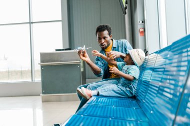 kız ve oğlu ile Afrika Amerikan babası havaalanında bekleme salonunda oturan ve oyuncak uçağı ile oynuyor 