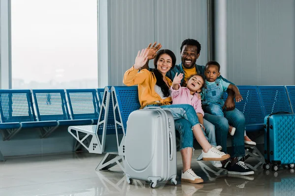 微笑的非洲裔美国家庭与行李和孩子坐在机场和挥舞双手在一起 — 图库照片