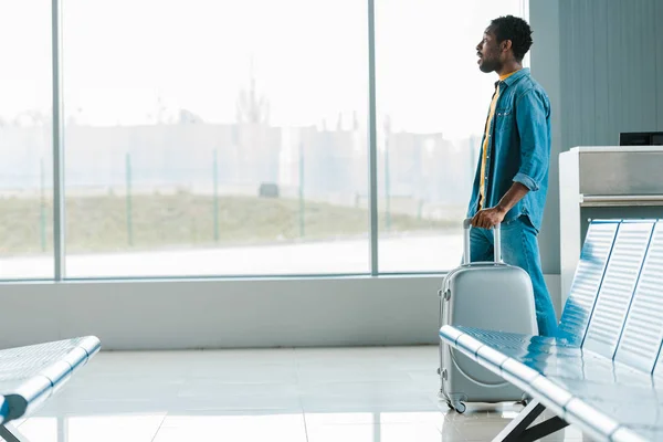 side view of african american man walking alone with suitcase in airport