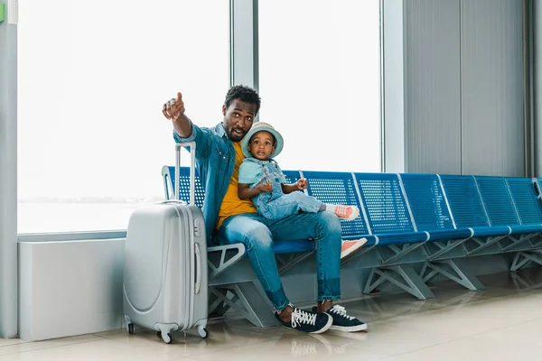 アフリカ系アメリカ人の父は 空港で息子と一緒に座って 指を離れて指さ — ストック写真
