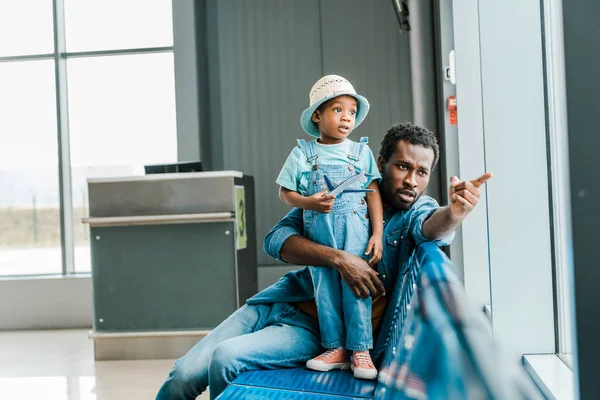 非洲裔美国父亲用手指指着窗口 而儿子在机场拿着玩具飞机 — 图库照片
