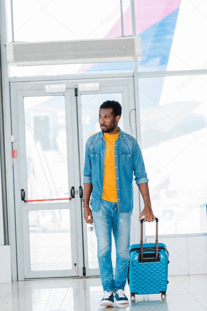 african american man walking with suitcase along waiting hall in airport