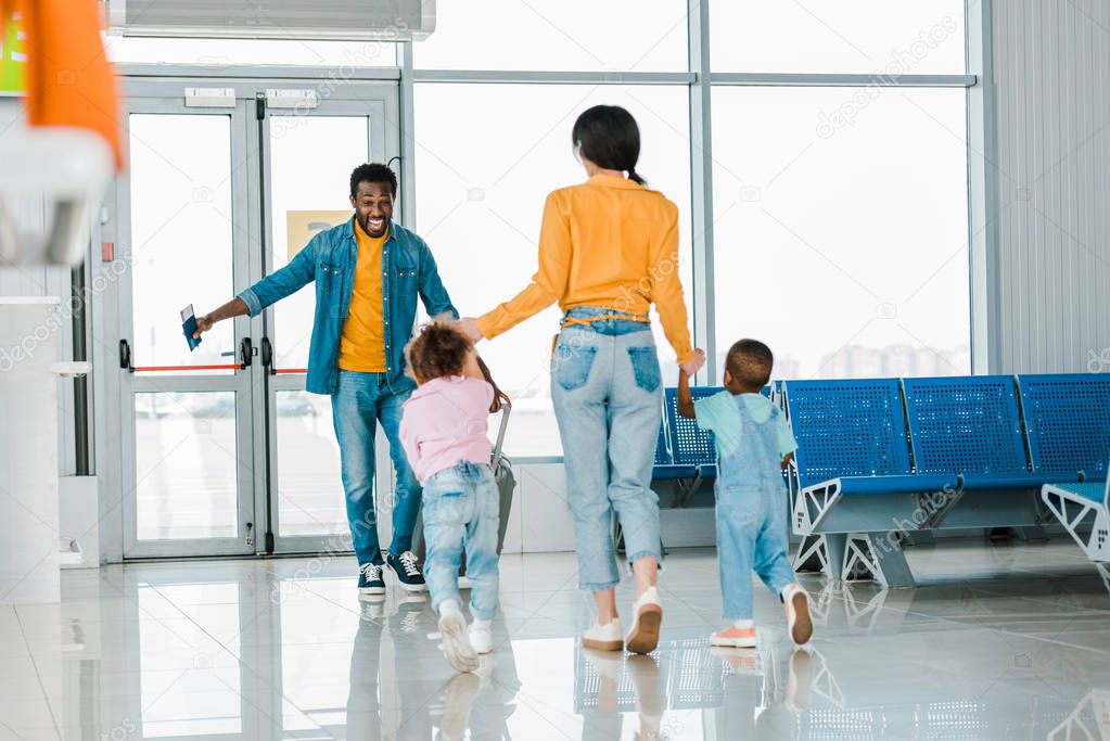 mother with children walking to happy african american man in airport