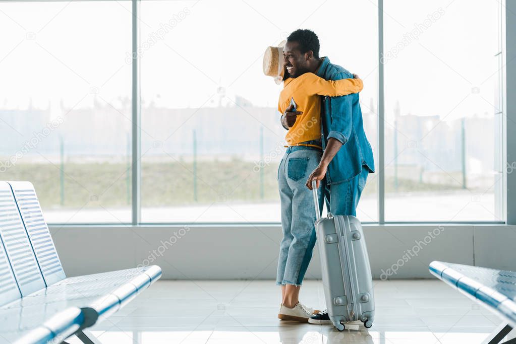 side view of happy african american man embracing girlfriend in airport