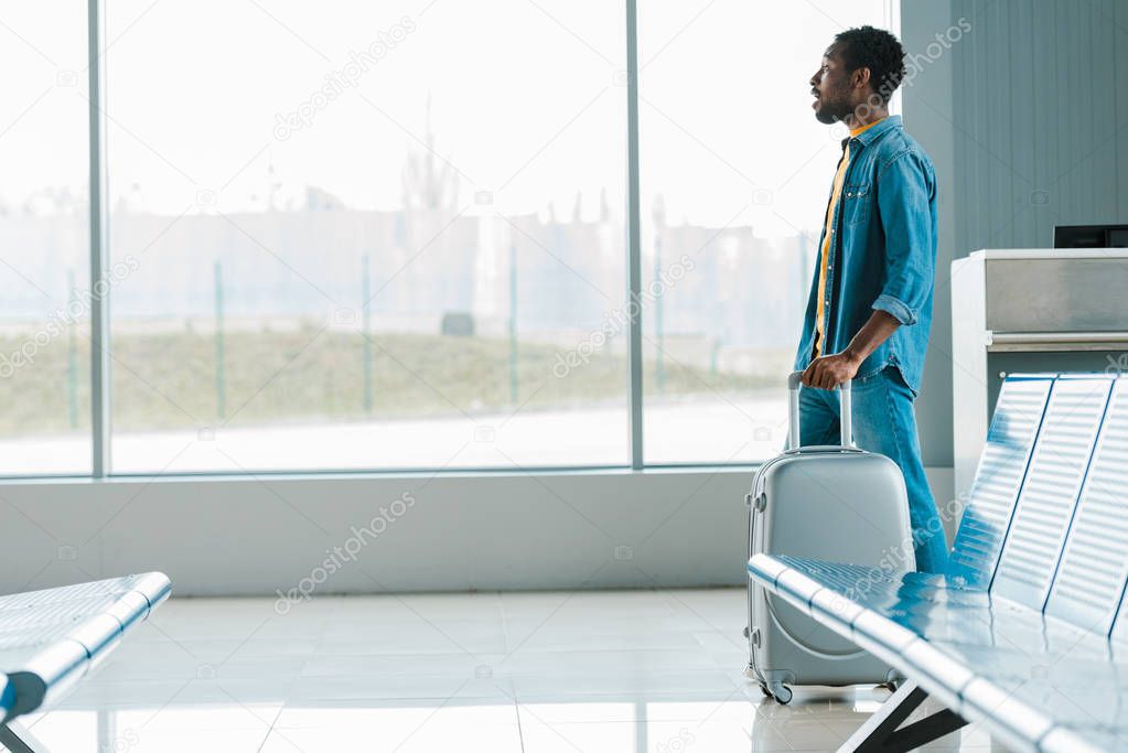 side view of african american man walking alone with suitcase in airport
