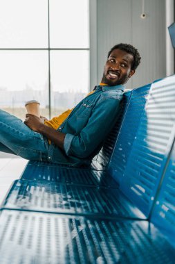 gitmek için kahve ile havaalanında oturan neşeli Afrikalı Amerikalı adam