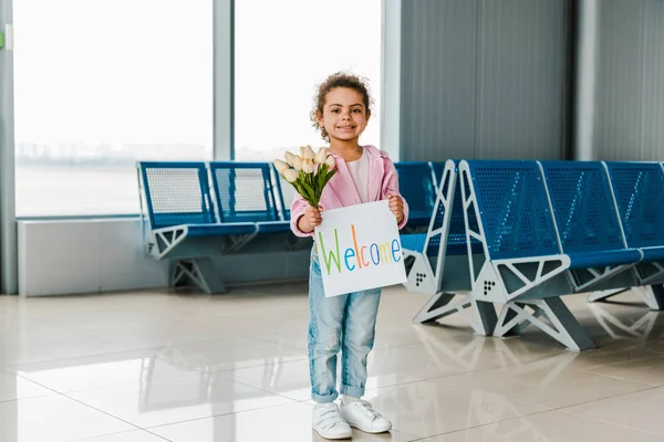 微笑的非洲裔美国孩子站在机场的等候大厅里 拿着郁金香和标牌 带着欢迎的字母 — 图库照片