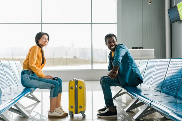 空港内のスーツケース付き出発ラウンジに座っている幸せなアフリカ系アメリカ人のカップルのサイドビュー — ストック写真