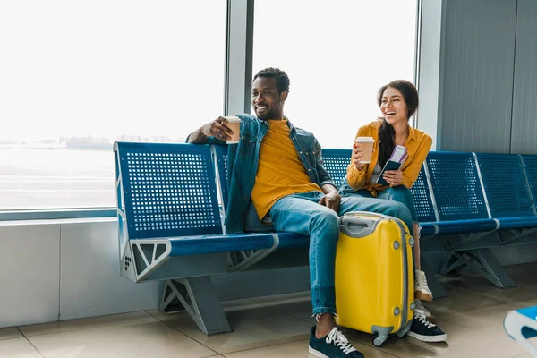 幸福的非洲裔美国夫妇坐在候机室与咖啡去和黄色旅行袋 — 图库照片