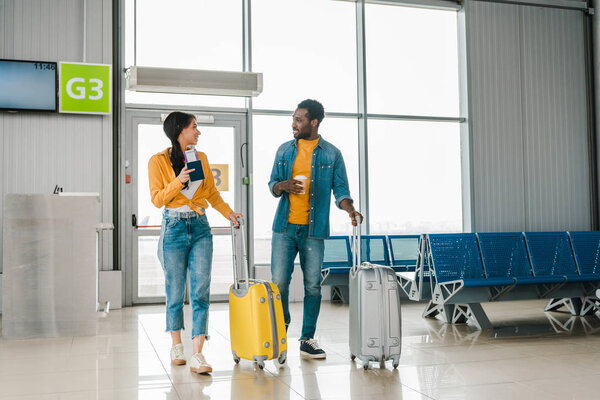 happy african american couple walking together in airport with travel bags