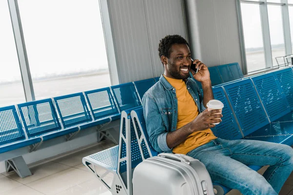 出発ラウンジで座っているとスマートフォンで話をしているアフリカ系アメリカ人男性の笑顔 — ストック写真