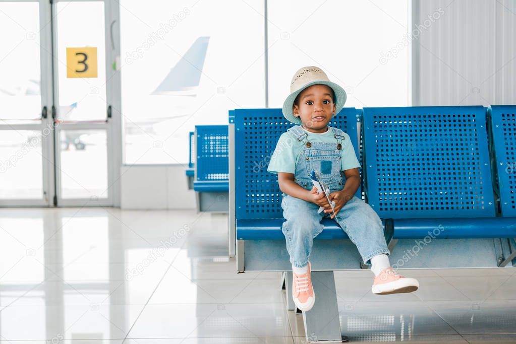 adorable african american boy sitting with toy plane in airport