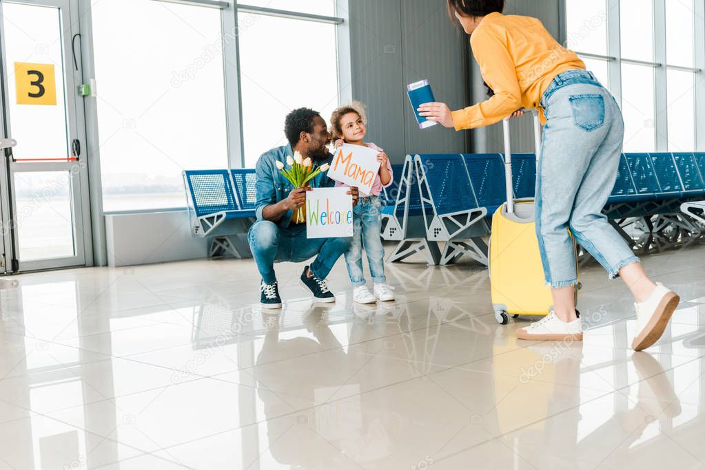 happy african american father and daughter meeting mother and wife with luggage in airport