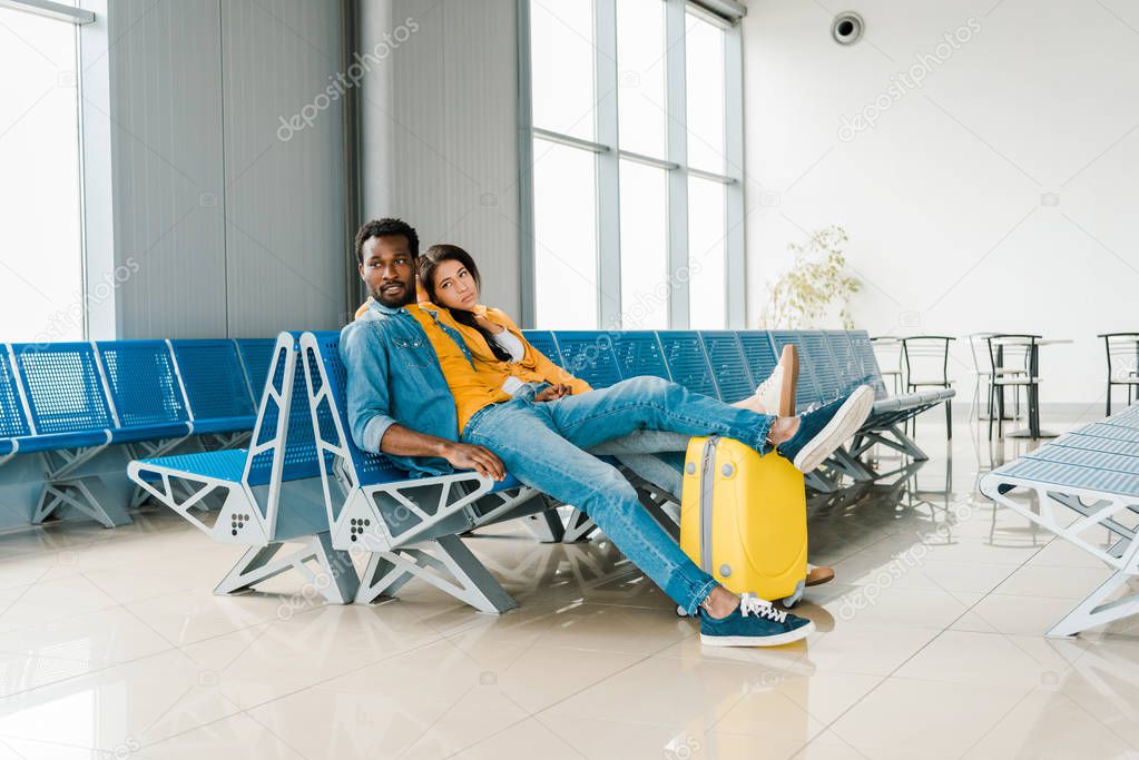 exhausted african american couple sitting in departure lounge with suitcase and waiting for flight