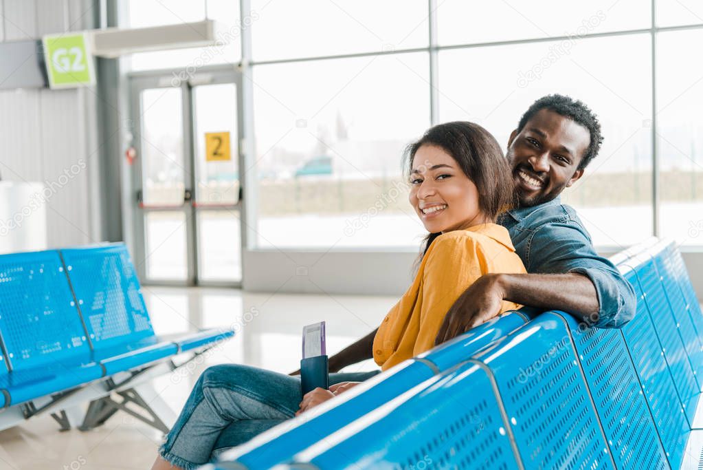 happy african american couple sitting in departure lounge with passports and air tickets