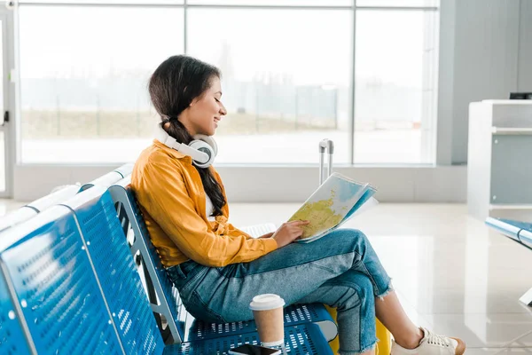 微笑的非洲裔美国妇女坐在耳机与咖啡去和地图在机场候机室 — 图库照片