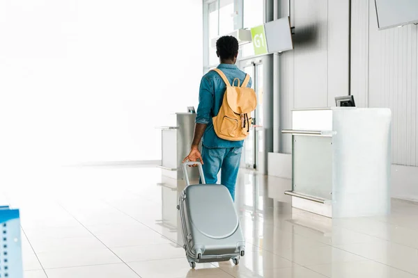 back view of african american man walking with baggage and backpack in airport