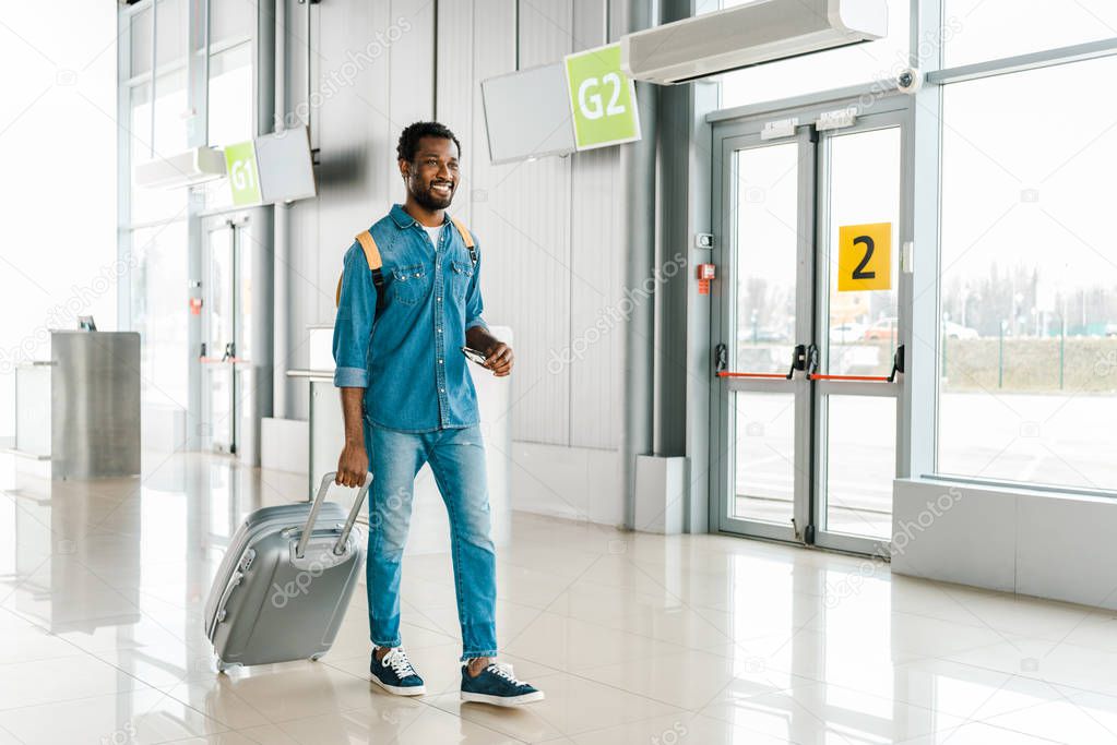 happy handsome african american man walking with suitcase in airport