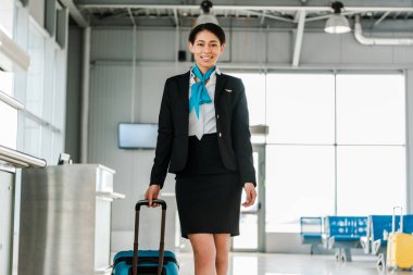 havaalanında bavul ile yürüyen çekici African American hostes gülümseyen
