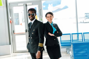 havaalanında birlikte ayakta çapraz silah ile güneş gözlüğü ve hostes gülümseyen Afrikalı Amerikan pilot