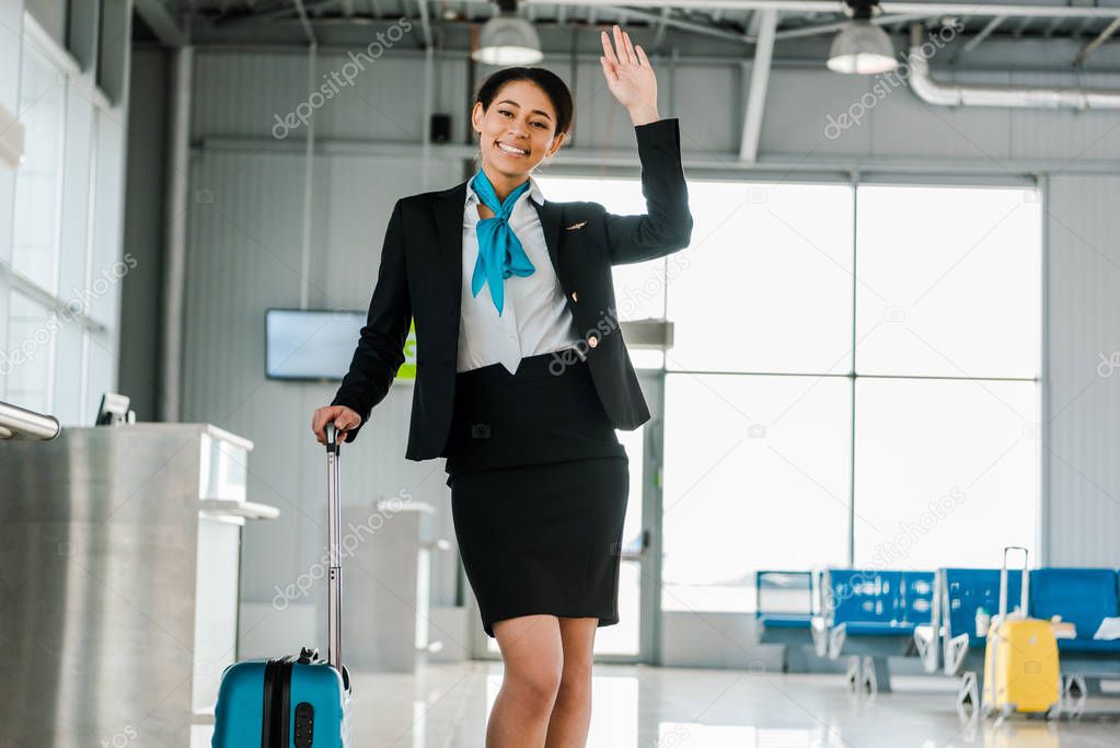 smiling african american stewardess waving hand in airport