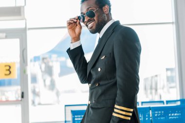 havaalanında kalkış salonunda güneş gözlüğü şık gülümseyen Afrikalı Amerikan pilot