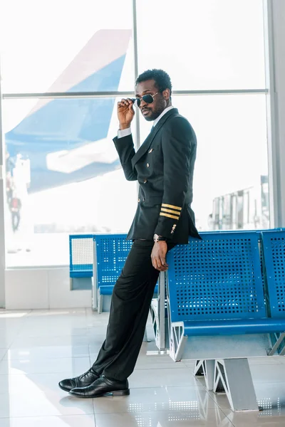 Впевнений Афроамериканський Пілот Сонцезахисних Окулярах Перехрещеними Ногами Залі Вильоту Аеропорту — стокове фото