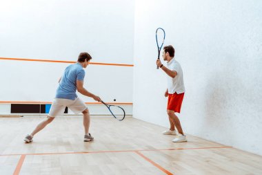 Dört duvarlı kortta squash oynayan iki sporcunun tam boy görünümü