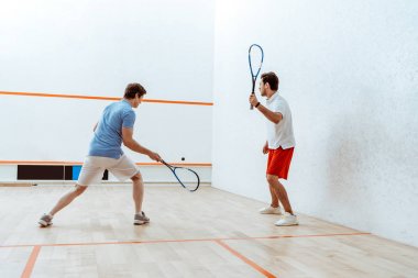 Full length view of two sportsmen playing squash in four-walled court clipart