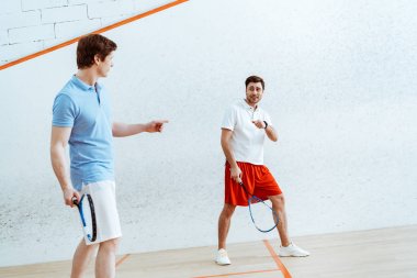 Squash oyuncularının birbirlerine bakıp parmaklarla işaret ederek tam uzunlukta görünümü