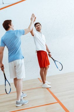 Dört duvarlı kortta yüksek beş işareti gösteren iki squash oyuncusu