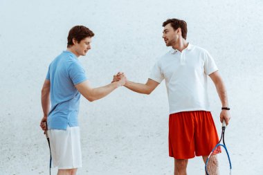 Raketleri ile el sıkışırken ve birbirlerine bakan iki squash oyuncusu