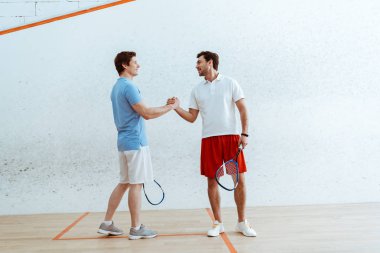 Raketleri ile el sıkışırken ve birbirlerine bakan iki squash oyuncusu